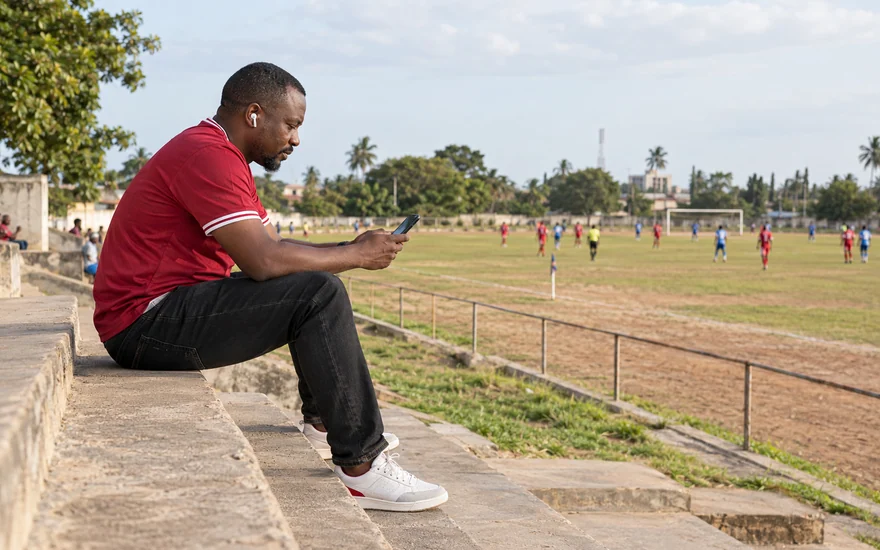 An adult spectator using a phone beside a local football pitch
