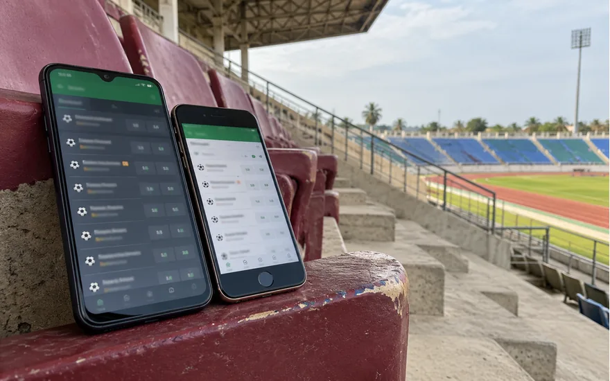Two older smartphones with blurred fixture lists rest on a stadium seat