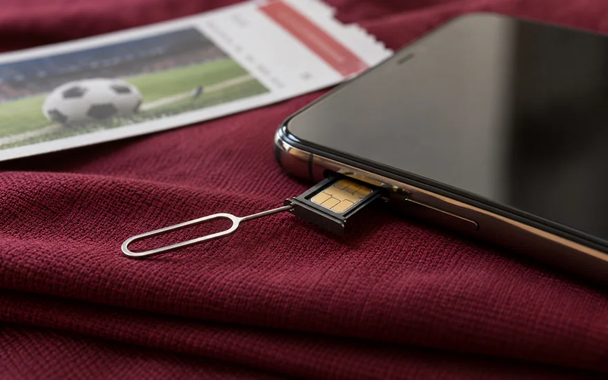 A SIM tray and eject tool beside a phone and a football ticket