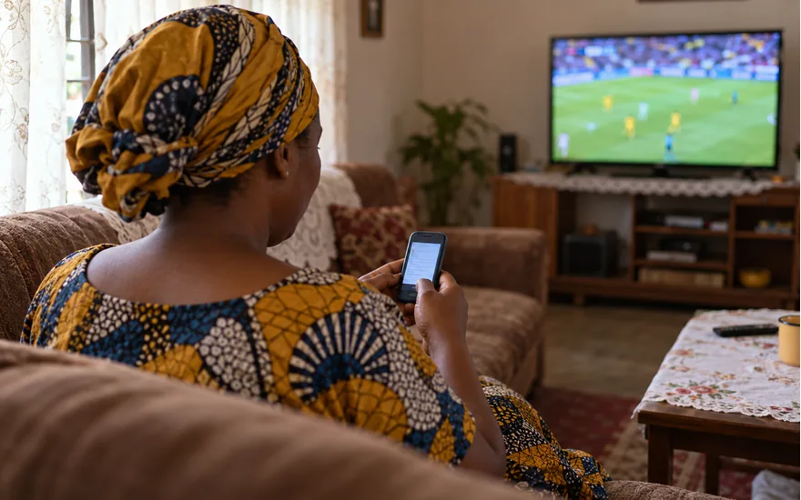An adult reads an SMS on a phone while football plays on a distant television